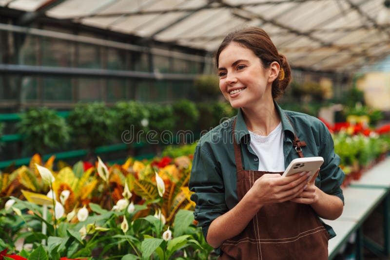 Jardinière souriante utilisant un téléphone portable pendant qu'elle travaille en serre photos libres de droits