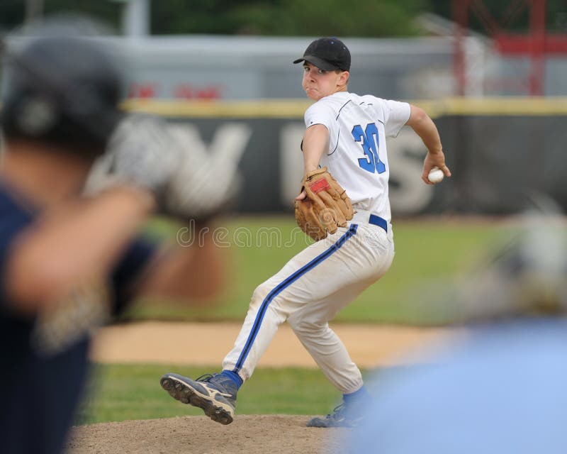 Caucasian high school baseball pitcher delivers pitch to batter while umpire looks on. Caucasian high school baseball pitcher delivers pitch to batter while umpire looks on