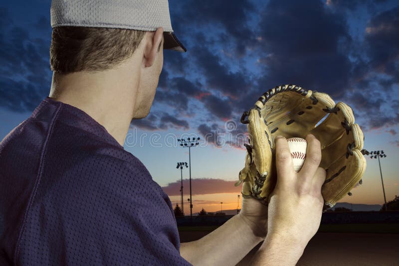 A close up view of the baseball pitchers hand just before throwing a fastball in a game. Focus on the fingers and the ball. Game being played just before sunset. A close up view of the baseball pitchers hand just before throwing a fastball in a game. Focus on the fingers and the ball. Game being played just before sunset