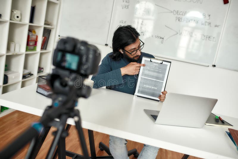 Javascript 在线。一位年轻人在家在线工作时，教授并解释 Java 的基础知识。正在录制视频教程 免版税图库摄影
