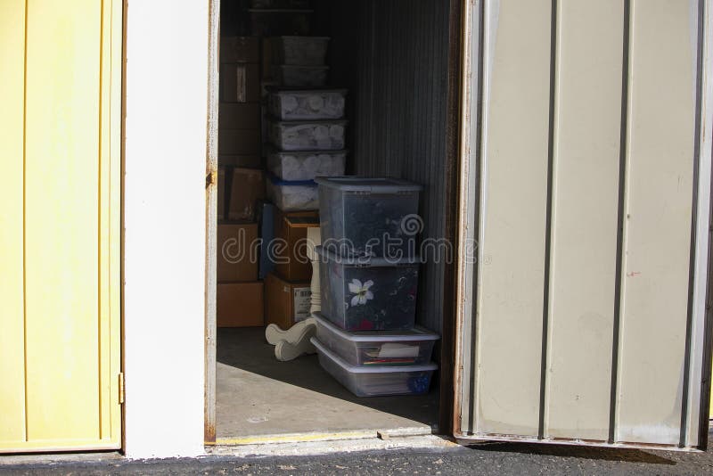 Close up of storage unit with furniture and cardboard and plastic boxes in a secure self storage facility with multiple drive up units. Open metal door. Close up of storage unit with furniture and cardboard and plastic boxes in a secure self storage facility with multiple drive up units. Open metal door.