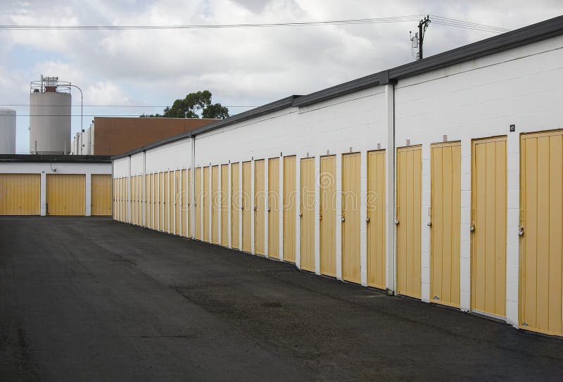 Building exterior of a secure self storage facility with multiple drive up units. Pad locked yellow metal doors. Building exterior of a secure self storage facility with multiple drive up units. Pad locked yellow metal doors.