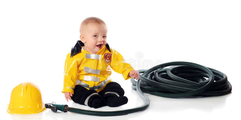And adorable baby boy winking while wearing a fireman's suit, wit his hat and hose nearby. Isolated on white. And adorable baby boy winking while wearing a fireman's suit, wit his hat and hose nearby. Isolated on white.