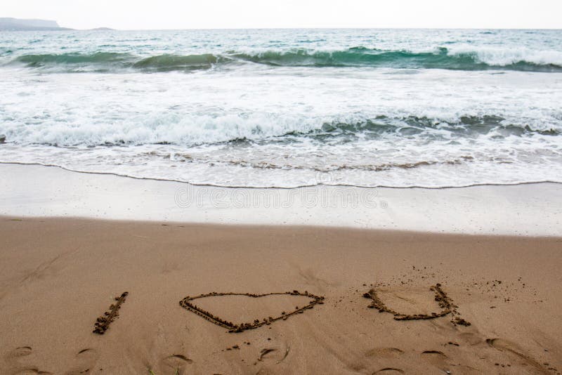 Je t'aime dessiné dans le sable d'une plage grecque avec de l'eau turquoise images libres de droits Je t'aime dessiné dans le sable d'une plage grecque avec de l'eau turquoise images libres de droits