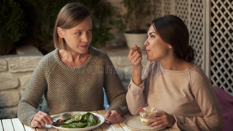 Jealous lady eating vegetable salad looking at friend tasting creamy dessert royalty free stock image Jealous lady eating vegetable salad looking at friend tasting creamy dessert royalty free stock image