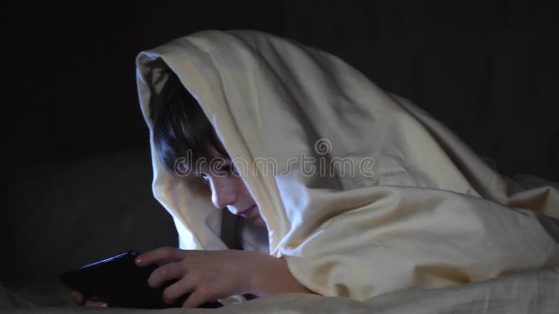 Jeden żartuje używać pastylka komputer osobistego pod koc przy nocą Chłopiec bawić się gry komputerowe