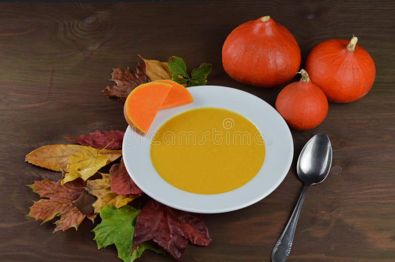 Jesienna dyniowa polewka w pucharze z hokkaido baniami, liśćmi i łyżką na brown drewnianym stole, zdjęcia stock Jesienna dyniowa polewka w pucharze z hokkaido baniami, liśćmi i łyżką na brown drewnianym stole, zdjęcia stock