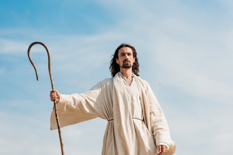 Jesus holding wooden cane against blue sky and clouds