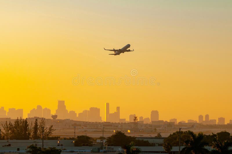 Jet airplane taking off from the Miami Florida airport with city skyline in background during sunrise, sunset.