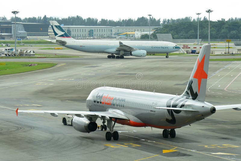 Jetstar Asia Airbus 320 che prepara per la partenza come taxi di Cathay Pacific Airbus 330 oltre fotografia stock libera da diritti Jetstar Asia Airbus 320 che prepara per la partenza come taxi di Cathay Pacific Airbus 330 oltre fotografia stock libera da diritti