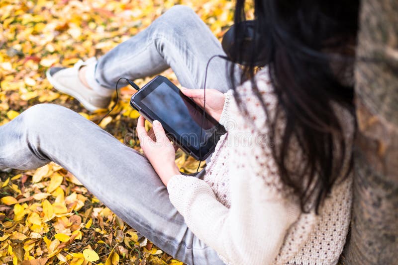 Jeune adolescente heureuse à l'aide de son comprimé et écoutant la musique dans le parc de ville d'automne Photo de mode de vie d images stock Jeune adolescente heureuse à l'aide de son comprimé et écoutant la musique dans le parc de ville d'automne Photo de mode de vie d images stock