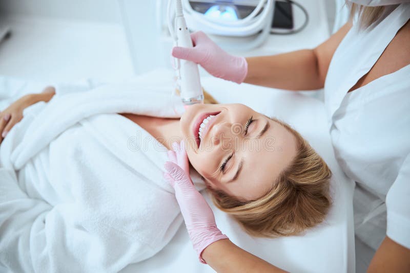 Top view of a joyous women being treated for neck lines by a qualified cosmetologist. Top view of a joyous women being treated for neck lines by a qualified cosmetologist