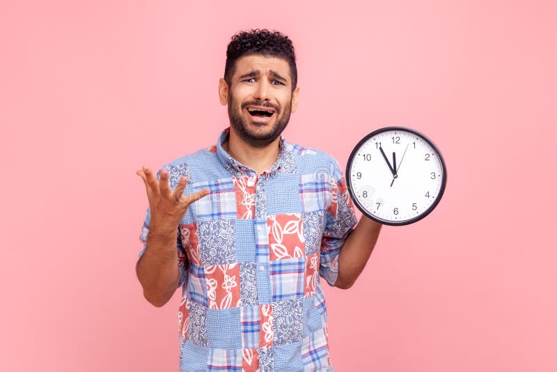 Jeune adulte mécontent homme à barbe nerveux avec cheveux foncés hurlant horloge murale à l'heure d'affichage en bleu casual photographie stock