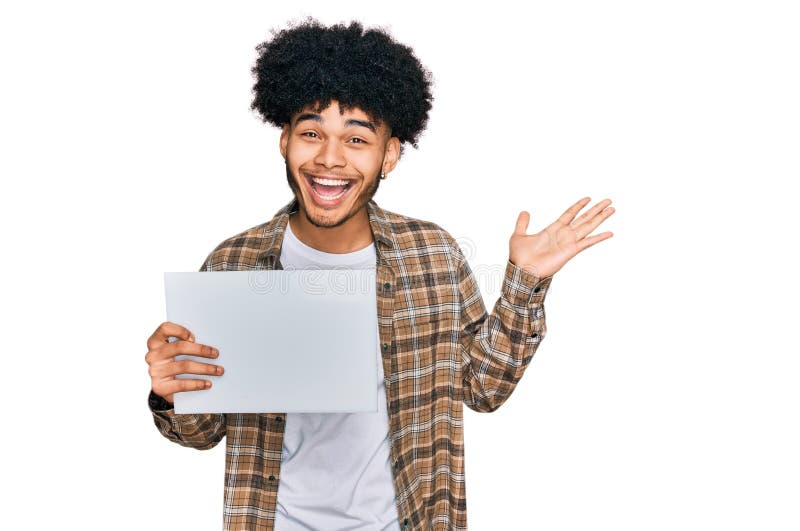 Jeune afro-américain aux cheveux afro tenant une bannière vierge célébrant la victoire avec un sourire heureux et l'expression du photo libre de droits