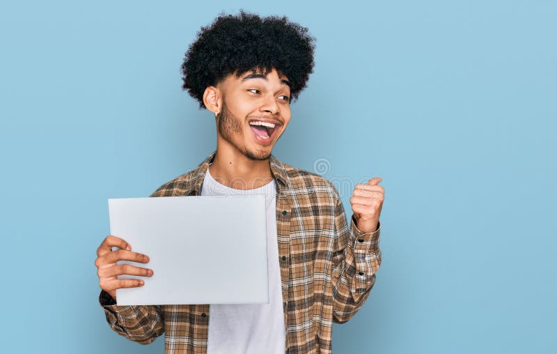 Jeune afro-américain aux cheveux afro tenant une bannière vierge pointant le pouce vers le côté souriant heureux avec la bouche ou images libres de droits