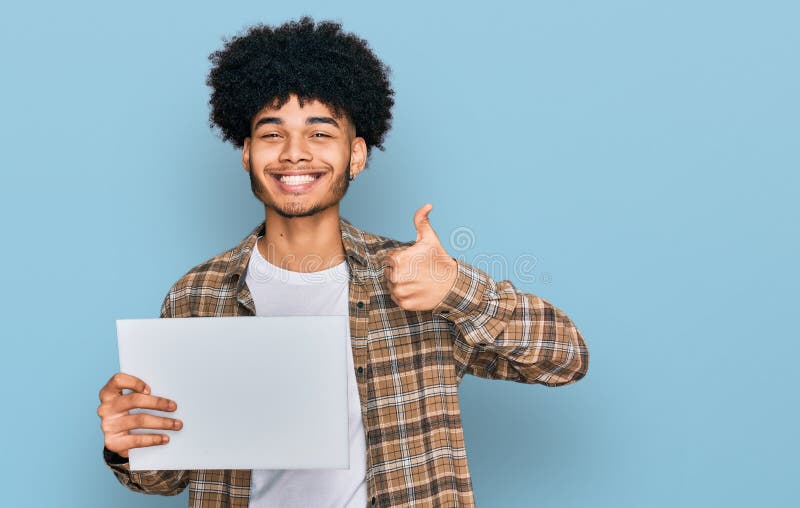 Jeune afro-américain avec cheveux afro tenant vide bannière souriant heureux et positif pouce en faisant excellent et image stock
