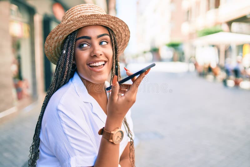 Jeune afro-américaine avec des tresses souriant heureux en utilisant un smartphone à l'extérieur, par un beau jour d'été image stock