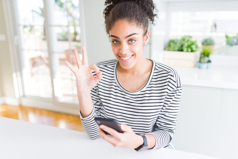 Jeune afro-américaine femme utilisant smartphone SMS un message faire ok signe avec les doigts excellent symbole photo stock
