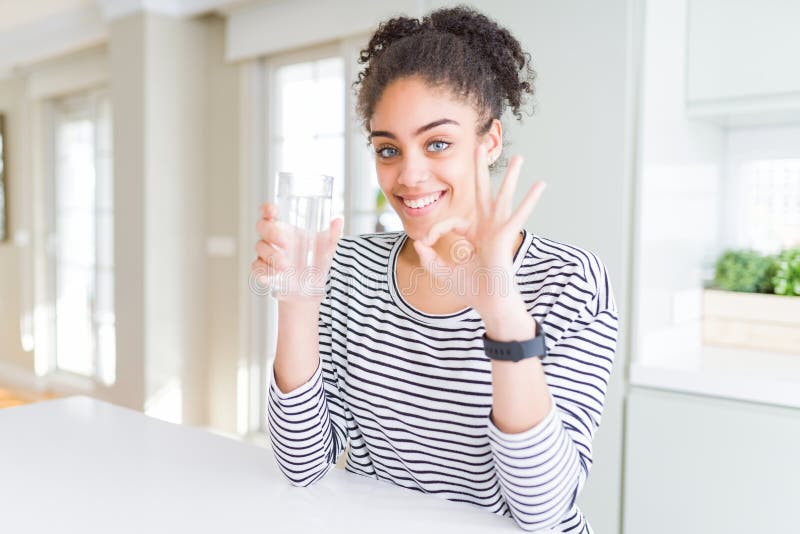 Jeune afro-américaine fille boire un verre d'eau frais faire ok signe avec les doigts excellent symbole image stock