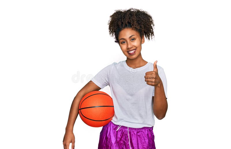 Jeune afro-américaine jouant au baseball tenant batte et balle souriant heureux et positif pouce vers le haut faisant excellent et photos libres de droits