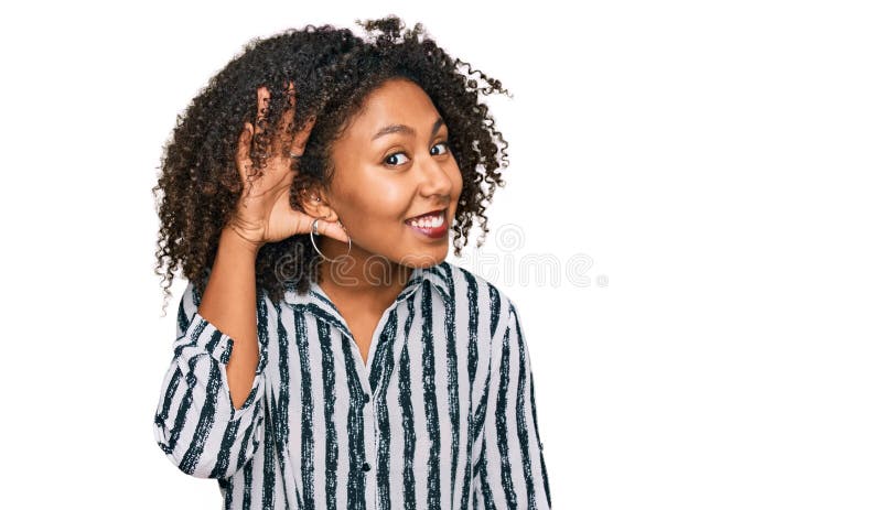 Jeune afro-américaine portant des vêtements décontractés souriant avec la main sur l'oreille écouter une rumeur ou commérages photographie stock libre de droits