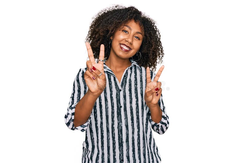 Jeune afro-américaine portant des vêtements décontractés souriant à la caméra montrant des doigts faisant signe de victoire photo stock