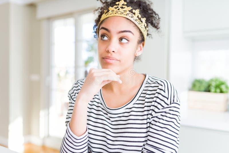 Jeune afro-américaine portant la couronne de reine d'or sur la tête avec la main sur le menton réfléchir à la question expression images libres de droits