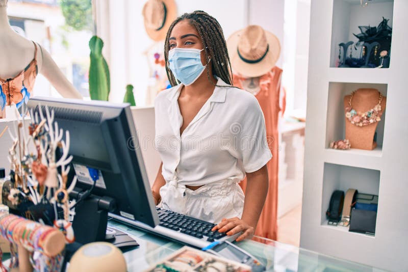 Jeune afro-américaine souriante heureuse travaillant au till portant un masque de sécurité coronavirus dans le magasin photographie stock