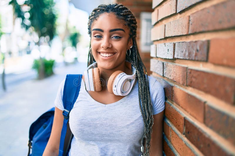 Jeune afro-américaine étudiante souriante heureuse assise sur le mur du campus universitaire photographie stock