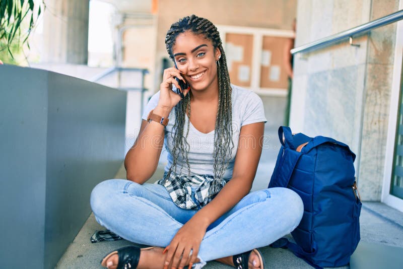 Jeune afro-américaine étudiante souriante heureuse en utilisant un smartphone sur le campus de l'université photos stock