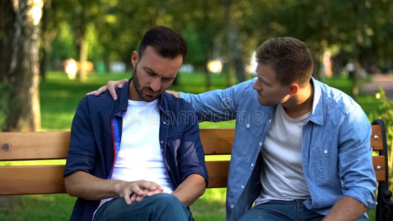 Young male supporting friend sitting outdoors together, friendship care, advice, stock photo. Young male supporting friend sitting outdoors together, friendship care, advice, stock photo