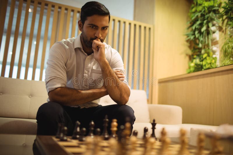 Jeune homme asiatique assis sur un canapé dans un salon moderne, analysant des pièces d'échecs en bois image libre de droits