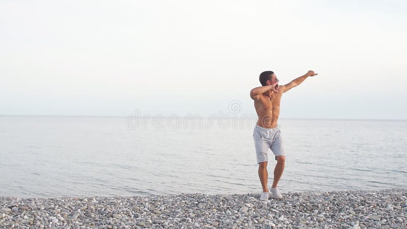 Jeune beau mâle mince sur la plage, danse, vacances d'été, ayant l'amusement, humeur positive