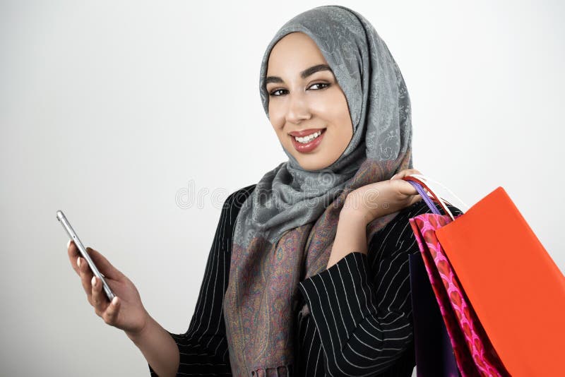 Jeune beau smartphone de port musulman de sourire de participation de foulard de hijab de turban de femme d'affaires dans un main image libre de droits Jeune beau smartphone de port musulman de sourire de participation de foulard de hijab de turban de femme d'affaires dans un main image libre de droits