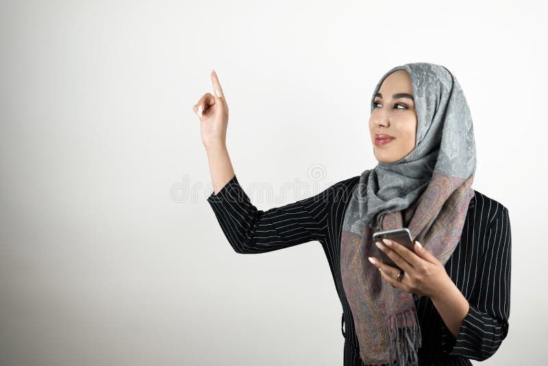 Jeune beau smartphone de port musulman de sourire de participation de foulard de hijab de turban de femme d'affaires à un main et images libres de droits Jeune beau smartphone de port musulman de sourire de participation de foulard de hijab de turban de femme d'affaires à un main et images libres de droits