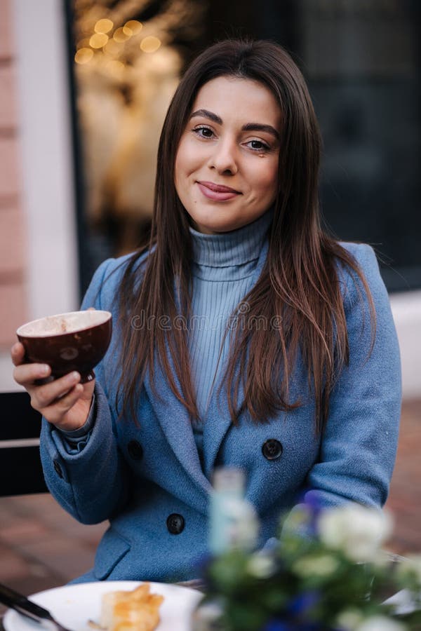 Jeune belle femme assise à l'extérieur dans le café et boire du café. femme heureuse en manteau bleu d'hiver. humeur de noël photo stock