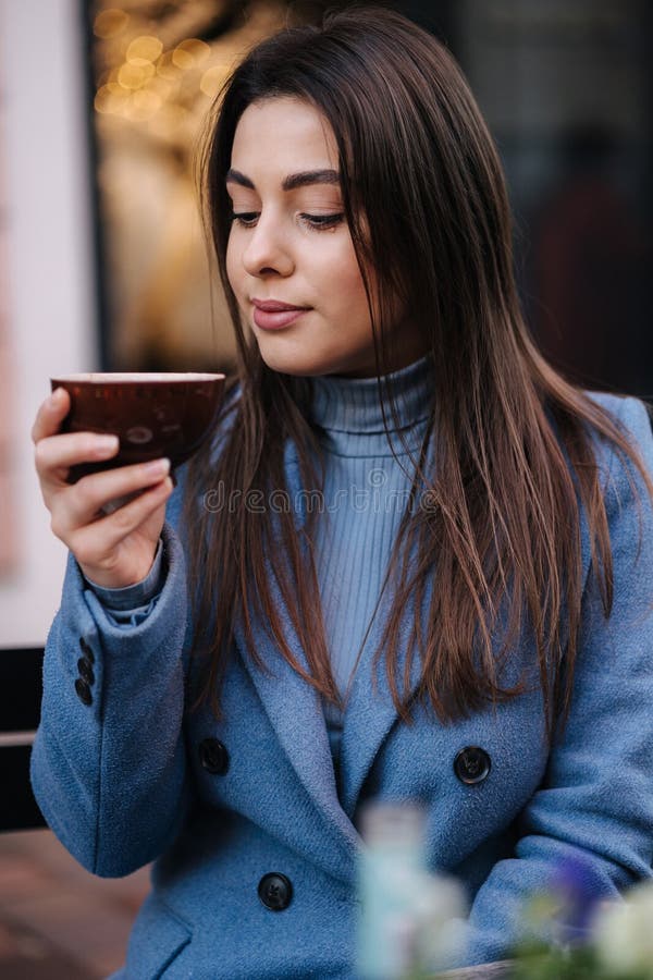 Jeune belle femme assise à l'extérieur dans le café et boire du café. femme heureuse en manteau bleu d'hiver. humeur de noël photo stock