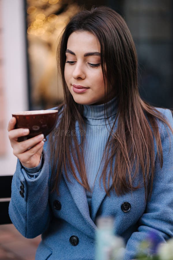 Jeune belle femme assise à l'extérieur dans le café et boire du café. femme heureuse en manteau bleu d'hiver. humeur de noël photos libres de droits