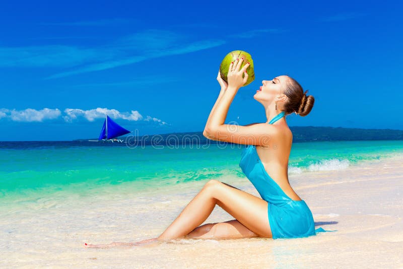 Jeune belle femme dans la robe bleue, l'eau potable de noix de coco sur t images stock Jeune belle femme dans la robe bleue, l'eau potable de noix de coco sur t images stock