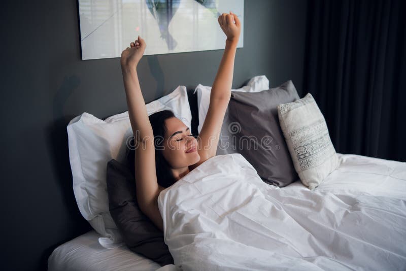 Young beautiful smiling and brunette woman lying in bed trying to wake up early morning stretching hands after sleep. Sweet dreams, good morning, new day, weekend, holidays concept. Young beautiful smiling and brunette woman lying in bed trying to wake up early morning stretching hands after sleep. Sweet dreams, good morning, new day, weekend, holidays concept