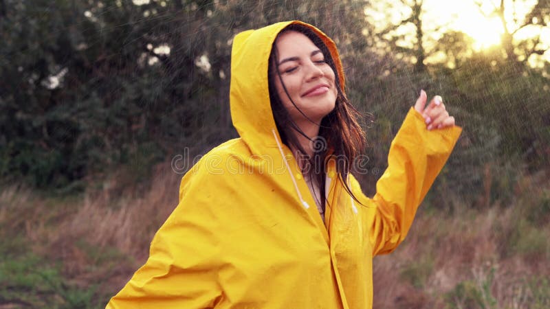 Jeune belle femme en imperméable jaune dansant sur le terrain et écoutant de la musique dans les écouteurs. fille profitant d'une banque de vidéos