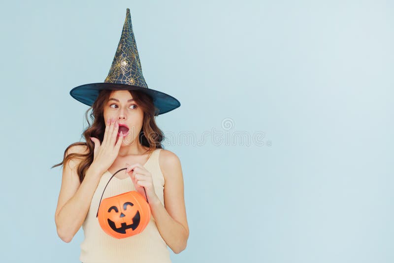 Young beautiful excited woman in a witch hat holds a basket pumpkin and looks away. Wow, Halloween sale. Young beautiful excited woman in a witch hat holds a basket pumpkin and looks away. Wow, Halloween sale.