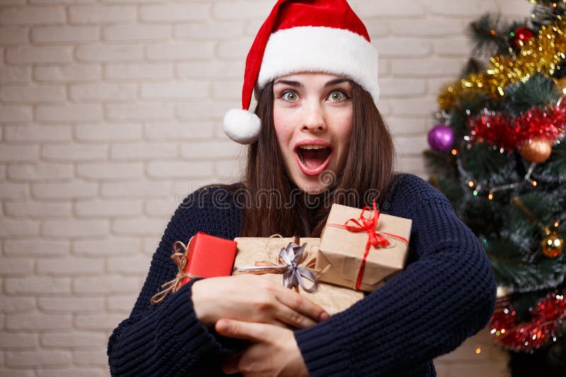 Jeune belle femme heureuse stupéfaite dans le chapeau de Santa avec des beaucoup cadeau b images libres de droits Jeune belle femme heureuse stupéfaite dans le chapeau de Santa avec des beaucoup cadeau b images libres de droits