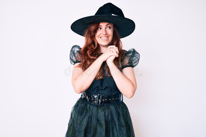 Young beautiful woman wearing witch halloween costume laughing nervous and excited with hands on chin looking to the side. Young beautiful woman wearing witch halloween costume laughing nervous and excited with hands on chin looking to the side