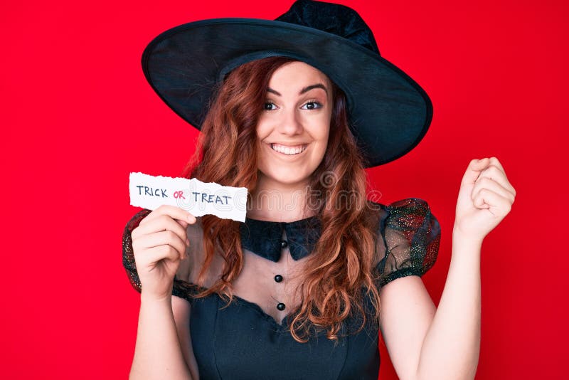 Young beautiful woman wearing witch halloween costume holding paper with trick or treat message screaming proud, celebrating victory and success very excited with raised arms. Young beautiful woman wearing witch halloween costume holding paper with trick or treat message screaming proud, celebrating victory and success very excited with raised arms