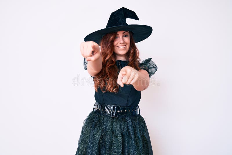 Young beautiful woman wearing witch halloween costume pointing to you and the camera with fingers, smiling positive and cheerful. Young beautiful woman wearing witch halloween costume pointing to you and the camera with fingers, smiling positive and cheerful