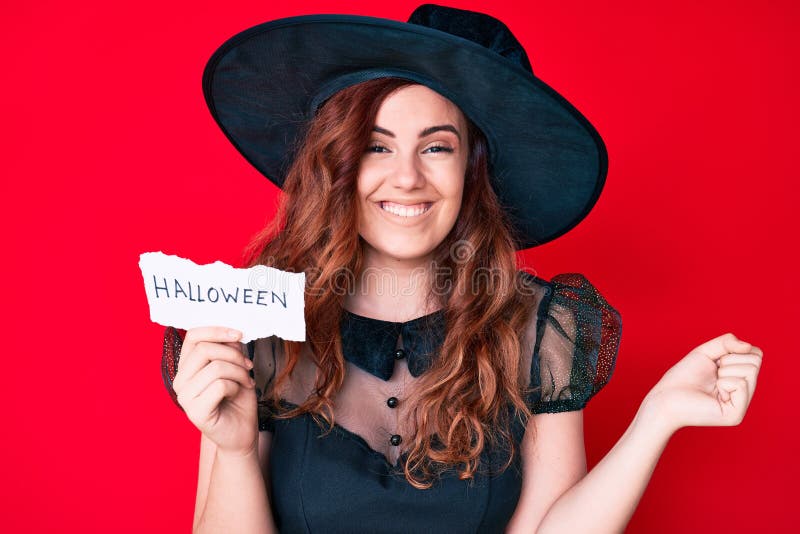 Young beautiful woman wearing witch halloween costume holding paper with halloween message screaming proud, celebrating victory and success very excited with raised arm. Young beautiful woman wearing witch halloween costume holding paper with halloween message screaming proud, celebrating victory and success very excited with raised arm