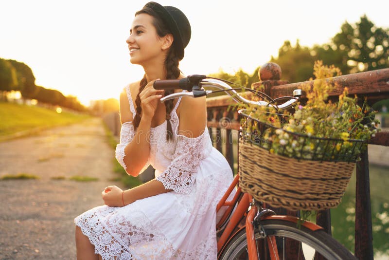 Jeune belle femme s'asseyant sur sa bicyclette avec des fleurs au soleil photos libres de droits Jeune belle femme s'asseyant sur sa bicyclette avec des fleurs au soleil photos libres de droits