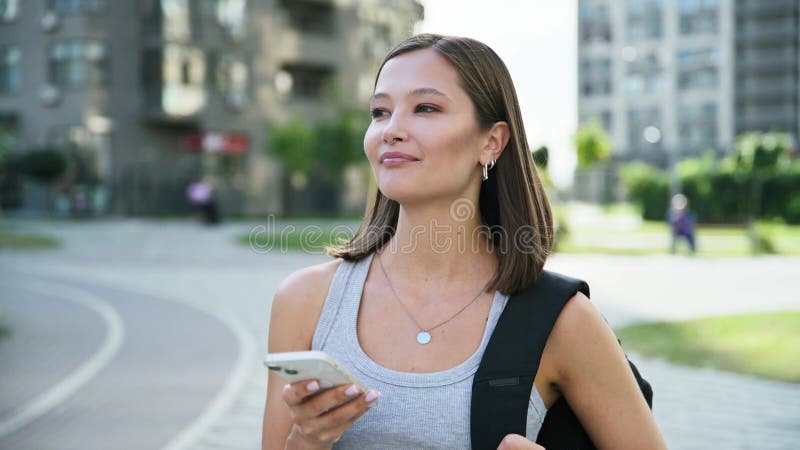 Jeune belle femme souriante avec sac à dos avec smartphone à l'extérieur clips vidéos