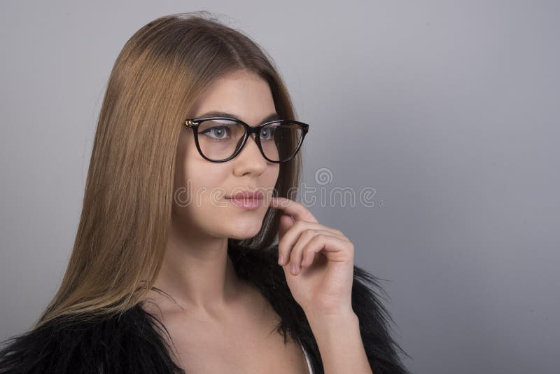 Jeune belle fille avec des verres se tenant devant le fond gris et regardant en avant, beaucoup d'espace propre photographie stock libre de droits Jeune belle fille avec des verres se tenant devant le fond gris et regardant en avant, beaucoup d'espace propre photographie stock libre de droits
